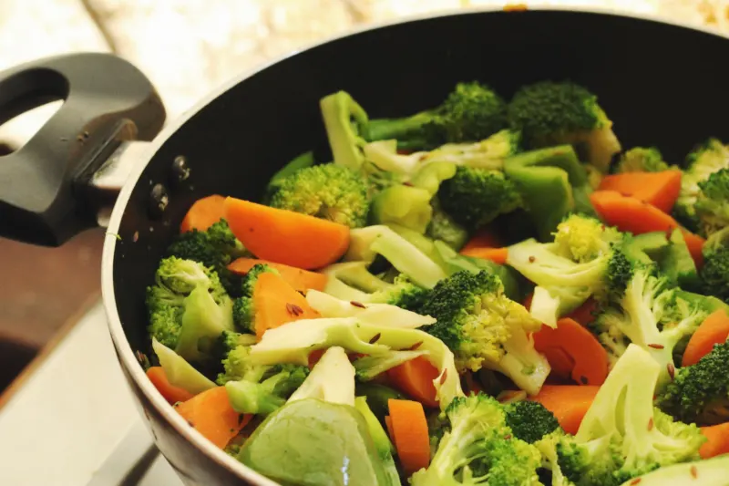 Broccoli, carrot, cabbage and green pepper pieces cooking in a black pan on a home hob