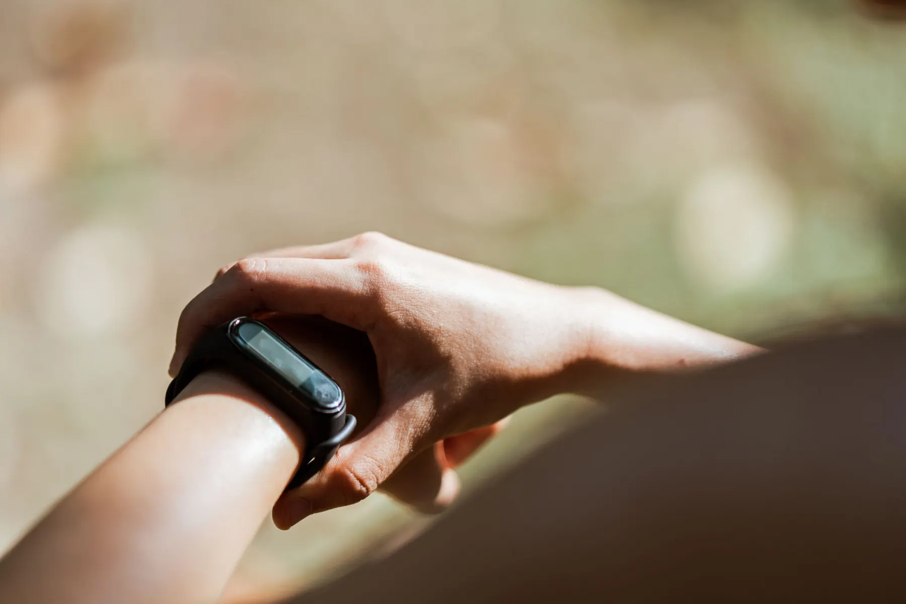 Close view of a wrist wearing a plain black fitness band, the other hand resting on it, in soft sunlight outdoors