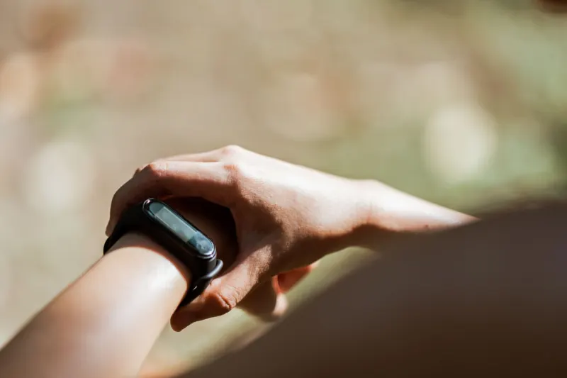Close view of a wrist wearing a plain black fitness band, the other hand resting on it, in soft sunlight outdoors